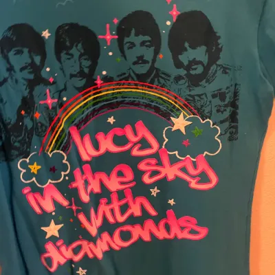 Sale Photo Thumbnail #133: Blue Beatles t-shirt featuring graphic portraits of the band above pink lettering that reads "Lucy in the sky with diamonds" with rainbow and star details.