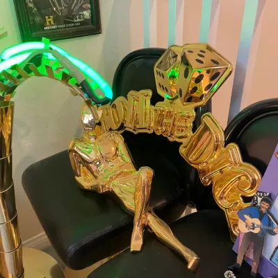 Sale Photo Thumbnail #150: Gold-tone "Roll the Dice" novelty sculpture featuring a reclining figure, dice graphics, and green neon lighting accents.