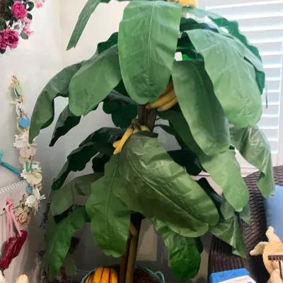 Sale Photo Thumbnail #163: Large artificial banana tree in a light blue woven basket, featuring realistic green leaves and yellow fruit clusters.
