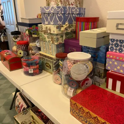 Sale Photo Thumbnail #176: Large assortment of decorative storage boxes, gift boxes, and craft ribbon spools displayed on folding tables.