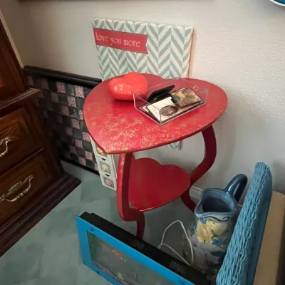 Sale Photo Thumbnail #106: Red heart-shaped two-tier side table with distressed gold finish, accompanied by various home decor items including a blue ceramic pitcher and framed art.