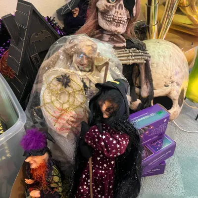 Sale Photo Thumbnail #159: Collection of Halloween decorations including witch figurines, a pirate skeleton prop, string lights in boxes, and a large skull prop.