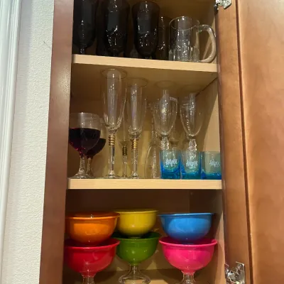 Sale Photo Thumbnail #28: Assorted glassware and colorful footed dessert bowls neatly arranged on shelves inside a wooden cabinet.