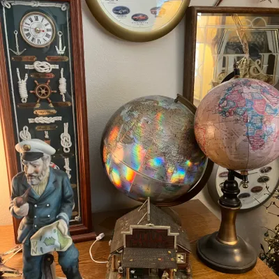 Sale Photo Thumbnail #208: Collection of nautical decor including a sea captain figurine, world globes, framed knot display board with clock, and a Chevrolet Corvette 50th Anniversary wall clock.