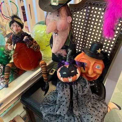 Sale Photo Thumbnail #155: Collection of whimsical Halloween figure decorations, including witch and jack-o'-lantern characters, arranged on a cane-back chair.
