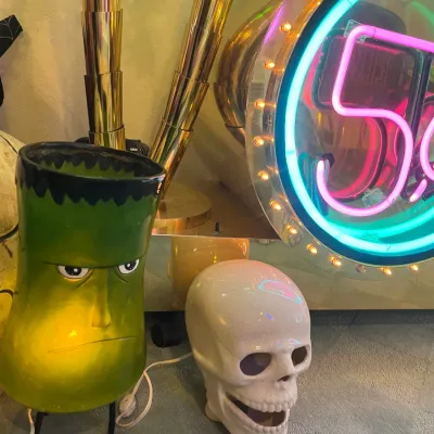 Sale Photo Thumbnail #156: Novelty Halloween decor assortment featuring an illuminated green Frankenstein monster lamp, a ceramic skull sculpture, and a neon 5¢ light sign.
