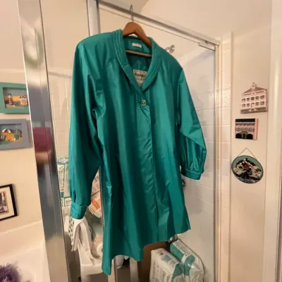 Sale Photo Thumbnail #131: Vintage emerald green satin or nylon coat featuring a shawl collar and single button closure, displayed on a wooden hanger.