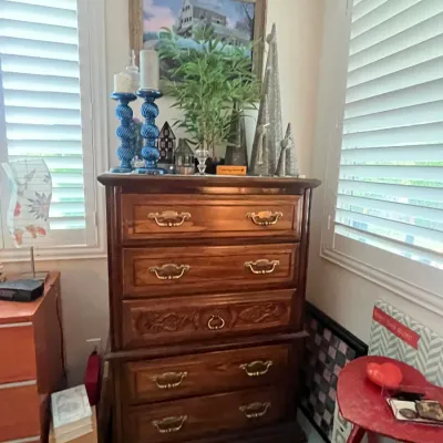 Sale Photo Thumbnail #107: Traditional oak five-drawer tall dresser with brass handles, styled with home decor accessories on top including candles, a framed picture, and artificial greenery.