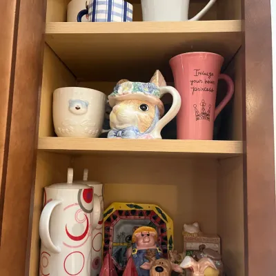 Sale Photo Thumbnail #15: Collection of novelty ceramic mugs, salt and pepper shakers, and figurines arranged inside a wooden kitchen cabinet.