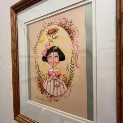 Sale Photo Thumbnail #126: Framed and matted Mary Engelbreit print titled 'To Mom With Love', housed in a natural wood frame.
