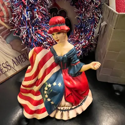 Sale Photo Thumbnail #76: Vintage ceramic Betsy Ross figurine in a patriotic dress styled after the American flag, displayed alongside red, white, and blue decorations.
