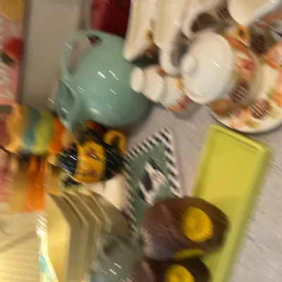 Sale Photo Thumbnail #21: Assorted vintage and modern kitchenware, including a light blue Fiesta pitcher, ceramic sugar and creamer sets, decorative signs, and yellow serving dishes.