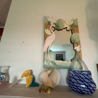 Sale Photo Thumbnail #114: Tropical-themed flamingo and water lily mirror mounted above a shelf featuring a ceramic toucan, a porcelain peacock, and an art glass purse vase.