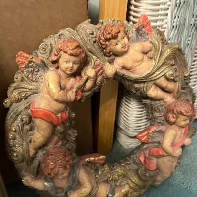Sale Photo Thumbnail #169: Vintage cherub wall plaque frame featuring ornate gold scrolls and hand-painted putti figures.