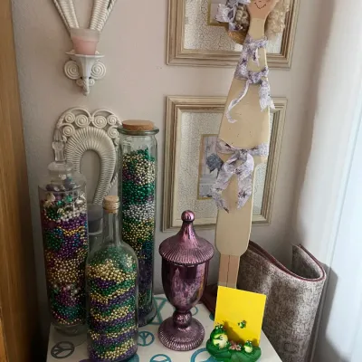 Sale Photo Thumbnail #185: Collection of decorative home accents, including glass jars filled with colorful beads, a purple mercury glass urn, and a handcrafted wooden doll figure, arranged on a table with peace sign decals.