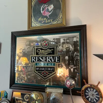 Sale Photo Thumbnail #200: Framed vintage Miller High Life and Miller Reserve Amber Ale advertising pub mirrors displayed above a collection of tabletop clocks.