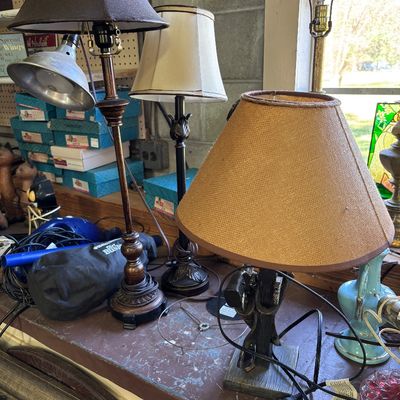 Sale Photo Thumbnail #76: Collection of assorted table lamps featuring various styles, including a dark wood turned column lamp, a metallic dark-finished base lamp with a white fabric shade, and a rustic lamp with a burlap shade.