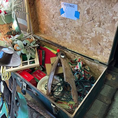 Sale Photo Thumbnail #34: Open vintage trunk filled with holiday decorations, including Christmas lights, boxed ornaments, festive ribbon, and a wooden reindeer.