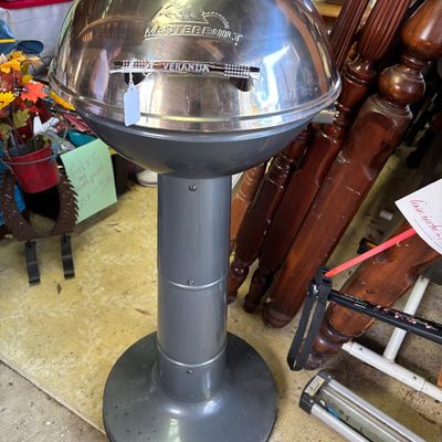 Sale Photo Thumbnail #32: Masterbuilt Veranda outdoor kettle grill with a stainless steel dome lid, built-in temperature gauge, and gray pedestal base.