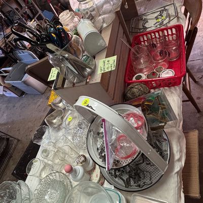Sale Photo Thumbnail #55: Assorted kitchenware display featuring clear glass jars, drinking glasses, cookie cutters in a vintage metal steamer, and craft supplies on a table.