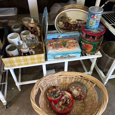 Sale Photo Thumbnail #89: Assortment of vintage collectibles, including German beer steins in a yellow plaid box, decorative holiday tins, a large serving tray with a horse carriage scene, and a large woven basket.