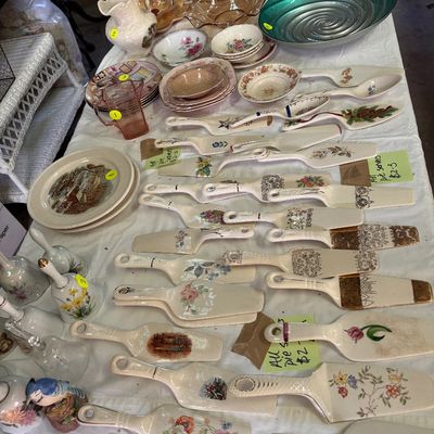 Sale Photo Thumbnail #66: Large collection of vintage porcelain and ceramic pie servers with floral patterns, alongside assorted glassware and tableware arranged on a display table.