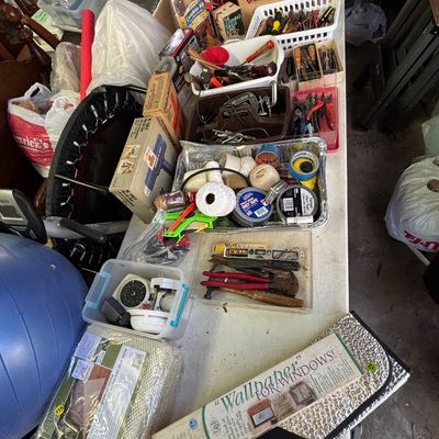 Sale Photo Thumbnail #27: Large collection of assorted household items, hand tools, tapes, hardware, and boxed goods laid out on a folding table.