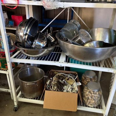 Sale Photo Thumbnail #87: White wire rolling shelving unit holding various metal cookware, large mixing bowls, baking pans, power cords, and glass jars full of corks.