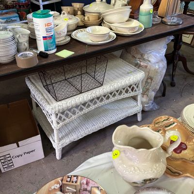Sale Photo Thumbnail #64: Assorted household goods and ceramics displayed on a wooden table, featuring white wicker shelving underneath and decorative tableware in the foreground.