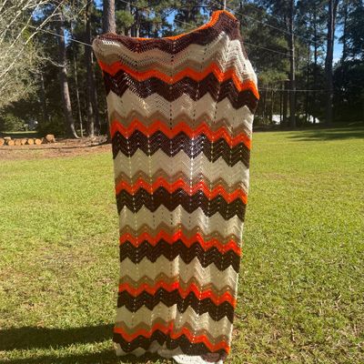 Sale Photo Thumbnail #7: Vintage 1970s crocheted chevron afghan blanket featuring stripes of orange, brown, tan, and cream.