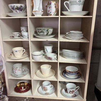 Sale Photo Thumbnail #75: Collection of vintage porcelain teacups, saucers, and small pitchers displayed in a white wooden cubby shelf.