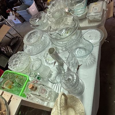 Sale Photo Thumbnail #56: Large assortment of vintage clear glassware, featuring serving bowls, decanters, pressed glass plates, and kitchenware arranged on a table.