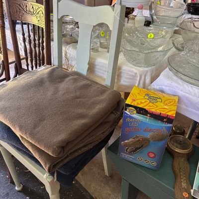 Sale Photo Thumbnail #43: Painted light-green wooden side chair holding folded wool blankets, alongside a boxed Banana Boat floating LED gator decoy and a vintage wooden wall barometer.