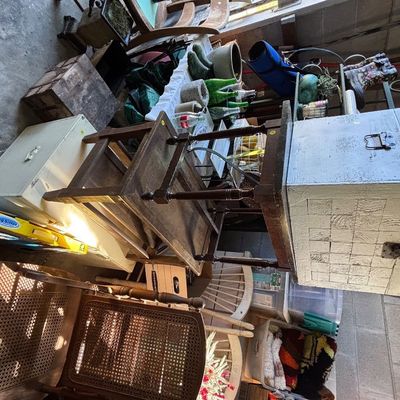 Collection of vintage furniture and household items, including a cane-back chair, stacked wooden tables, and rustic storage trunks.