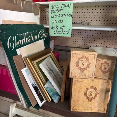 Sale Photo Thumbnail #84: Selection of framed wall art, local event posters, and boxed Yesterday's Child collectible figurines displayed on shelving.