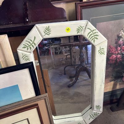 Sale Photo Thumbnail #82: Octagonal wall mirror featuring a distressed white painted frame with hand-painted green leaf motifs, surrounded by various framed artworks.