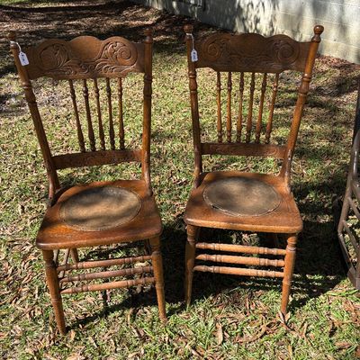Sale Photo Thumbnail #92: Pair of antique press-back oak dining chairs with carved scroll tops, spindle backs, and inset leather-look round seat cushions.