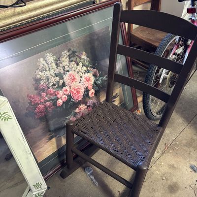 Sale Photo Thumbnail #80: Dark brown ladder-back child's rocking chair with a woven seat, shown in front of a framed floral art print.