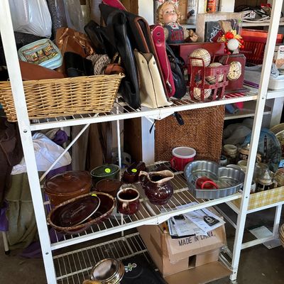 Sale Photo Thumbnail #93: White wire shelving unit filled with various household items, including handbags, a porcelain doll, vintage brown pottery, and a heart-shaped baking pan.