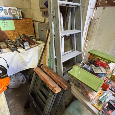 Sale Photo Thumbnail #25: Vintage painted grey wooden stepladder alongside folding sawhorses and assorted workshop hand tools.
