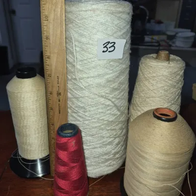 Sale Photo Thumbnail #50: Assortment of five industrial thread cones and yarn spools in varying neutral and red shades, shown next to a wooden Westcott ruler for scale.