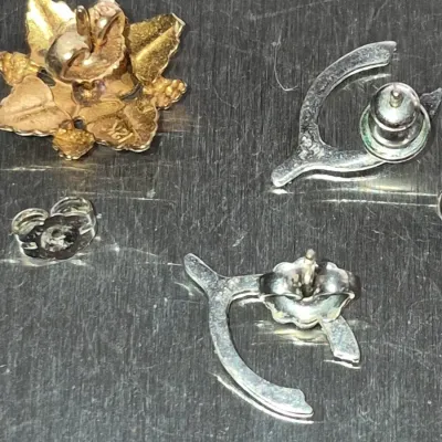 Sale Photo Thumbnail #845: Small assortment of fine jewelry pieces including a pair of silver wishbone post earrings, a 12K gold leaf-motif earring or pin back, and a loose earring clutch.