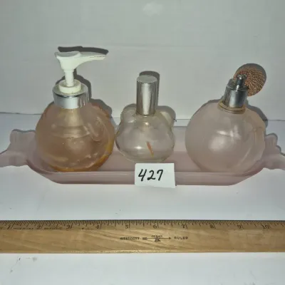 Sale Photo Thumbnail #745: Vintage frosted pink glass vanity set featuring three perfume bottles and a matching tray, shown next to a 12-inch ruler for scale.