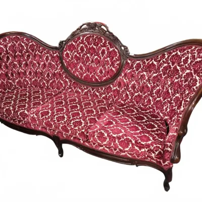 Sale Photo Thumbnail #106: Victorian-style camelback sofa with carved dark wood frame and red patterned velvet upholstery.