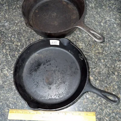Sale Photo Thumbnail #650: Pair of vintage cast iron skillets showing signs of age and wear, including surface rust and seasoning build-up.