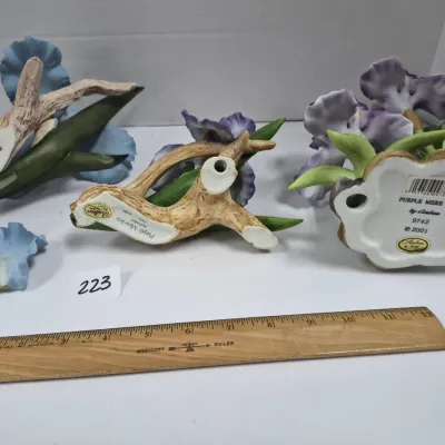 Sale Photo Thumbnail #385: Collection of three Andrea by Sadek porcelain floral figurines depicting irises, showing undersides with maker labels alongside a detached petal.