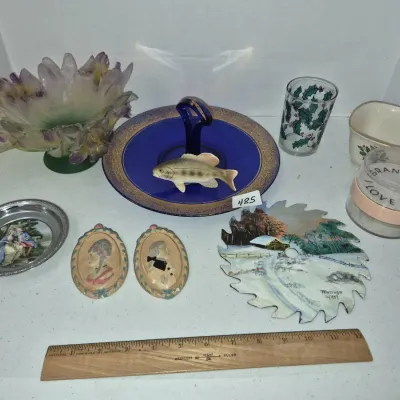 Sale Photo Thumbnail #832: Collection of decorative collectibles including a painted circular saw blade, cobalt blue centerpiece handle plate with a fish figurine, a floral art glass bowl, and small framed portraits.