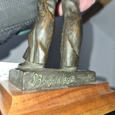 Sale Photo Thumbnail #759: Detail of a bronze figurine depicting a figure's legs, signed 'S. Bleifeld '86' on the base and mounted on a wooden display stand.