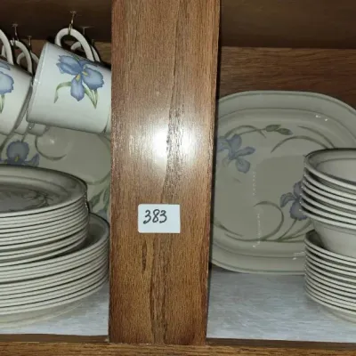 Sale Photo Thumbnail #669: Set of Pfaltzgraff Moonlight dinnerware inside a cabinet, featuring a blue iris pattern on off-white ceramic, including plates, bowls, platters, and hanging mugs.
