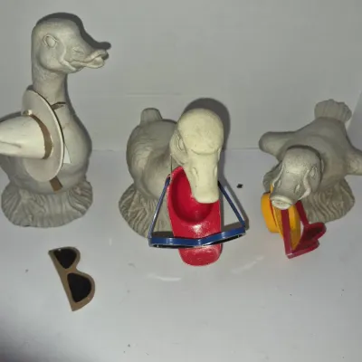 Sale Photo Thumbnail #785: Trio of vintage duck garden statues or figurines depicted holding tiny hats and sunglasses in their bills.